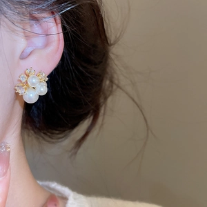 Elegant gold plated pearl flower earrings with zircons shown on a female ear model