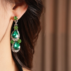 Detailed view of luxury silver-tone drop earrings with green teardrop crystals on model