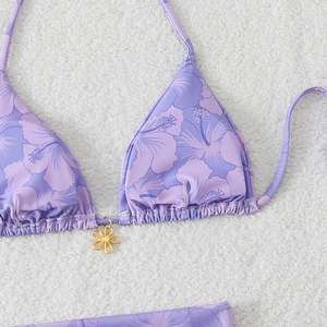 Detail of purple floral bikini top with gold flower charm on a soft white background