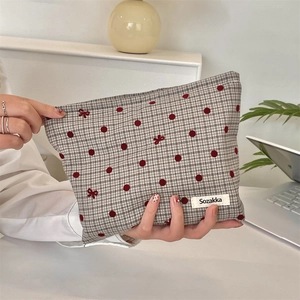 Close-up of gray polka dot makeup bag with red bow embroidery and woven logo label
