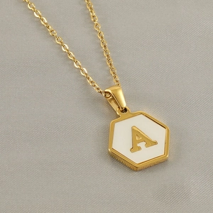 Macro view of gold hexagonal pendant with white inlay and golden letter A on chain