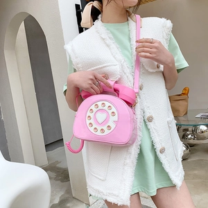 Pink vintage telephone-shaped crossbody bag in glossy patent leather shown on model