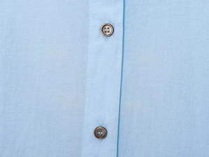 Detail view of light blue shirt featuring cotton texture and brown buttons close-up