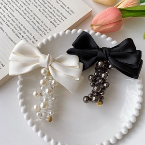 Elegant satin bow hair clips with pearls in black and cream on decorative white plate