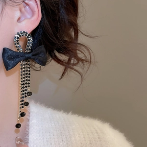 Close-up of black bow earrings with diamond tassels hanging elegantly on an ear