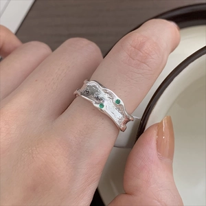 Close-up of irregular textured S925 silver ring with small green gemstones on finger
