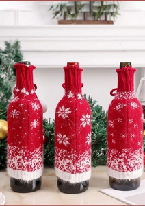 Close-up of three red knitted wine bottle covers with white snowflake patterns on a table