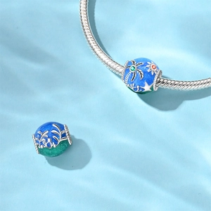 Macro view of blue and green enamel bead featuring silver palm trees and ocean waves