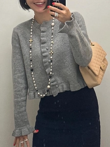 Close-up of grey knitted cardigan with ruffled trim details and pearl cross necklace