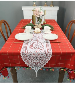 Detailed close-up of a white lace table runner with tassels on a red checkered tablecloth
