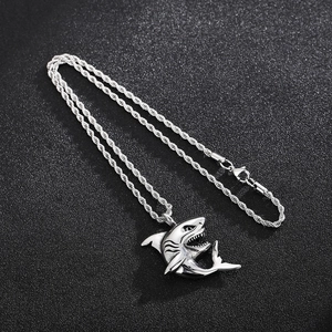 Detailed top view of a silver shark pendant on a twisted rope chain over a dark background