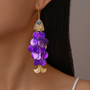 Close-up of long fish-shaped gold earrings with purple shell scales and blue evil eye detail