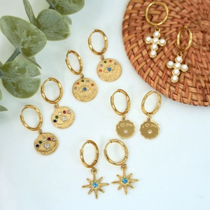 Detail view of gold hoop earrings with evil eye, cross, and star charms on a white background