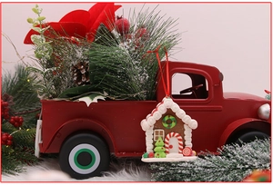 Close-up of red vintage truck with gingerbread house charm and festive pine needles