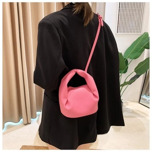 Detail of a bright pink ruched cloud bag with a knotted handle worn by a model
