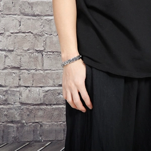 Polished silver stainless steel Cuban link bracelet worn on wrist against a brick wall