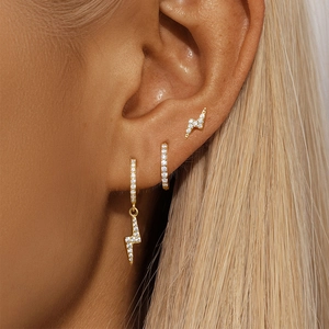 Close-up of gold-plated lightning bolt earrings set with zircon stones on female ear