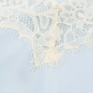 Detailed macro view of delicate ivory eyelash lace trimming on light blue fabric