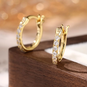 Elegant gold hoop earrings with sparkling white cubic zirconia on a luxury wooden base