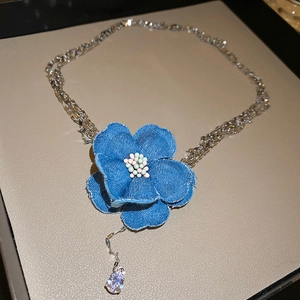 Détail macro du collier fleur en denim avec pendentif en zircon sur chaînes multicouches