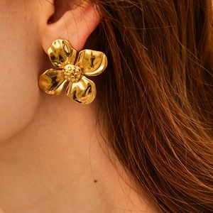 Close-up of a 3D gold flower earring with a polished finish worn by a model