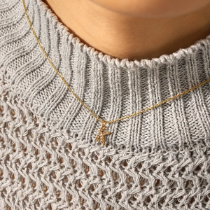 Collier en acier inoxydable doré avec pendentif lettre K en strass porté sur un pull gris