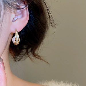 Detailed view of a C-shaped gold earring with zircon pave and a white pearl on an ear