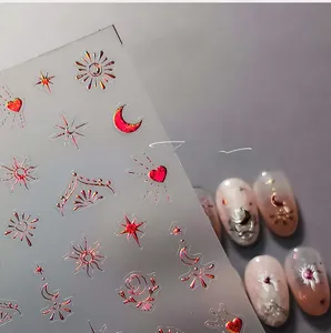 Detail of red and gold laser nail stickers with celestial sun, moon, and star patterns
