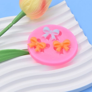 Pink silicone mold featuring three bow tie cavities for fondant and clay cake decoration