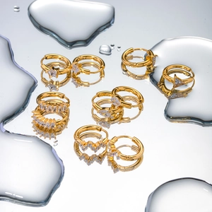 Artistic close-up of gold hoop earrings with teardrop zircons on a water drop surface