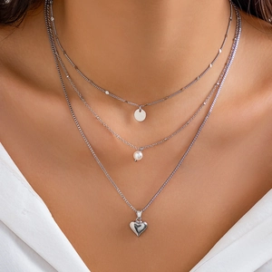 Detailed view of triple-layer silver necklace with heart, pearl and disc pendants