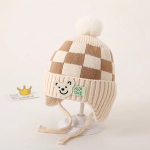 Detail van gebreide babymuts met oorkleppen, ruitpatroon en schattige beren-patch