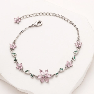 Detailed macro of silver cherry blossom bracelet with pink zircons and green leaves