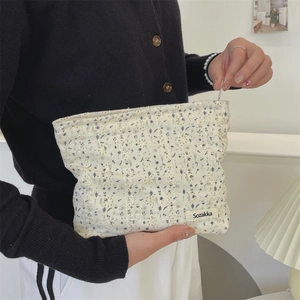 Detail of floral embroidery on cream canvas makeup bag with small zip and brand tag
