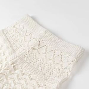 Macro shot of cream white knitted fabric showing geometric hollow patterns and ribbed cuffs