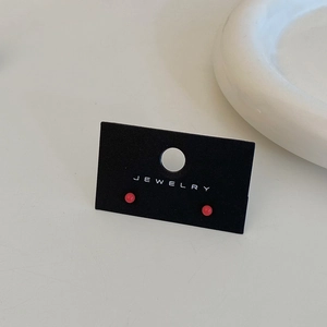 Close-up of vibrant coral red bean stud earrings displayed on a black jewelry card