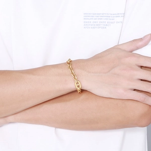 Detail of a gold Cuban link chain bracelet with a pig nose anchor pendant on person's wrist
