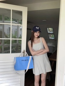 Detail of blue woven straw tote bag with black PARIS embroidery and long shoulder straps