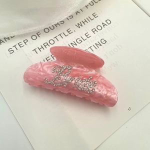 Close-up of pink acetate hair claw clip featuring sparkling rhinestone Bride lettering