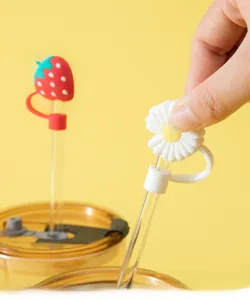 Detailed view of silicone strawberry and daisy straw covers on a bright yellow backdrop