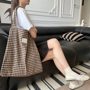 Detailed view of the checkered canvas shoulder bag worn by a model on a leather sofa