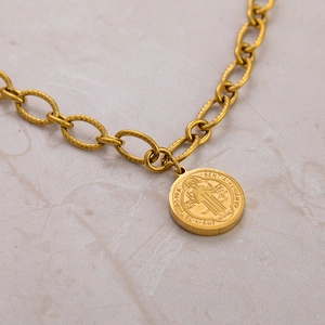 Macro shot of gold St. Benedict medal pendant with detailed religious relief on links