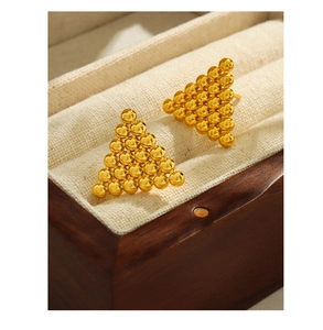 Macro detail of geometric triangle earrings with gold bead texture on a jewelry tray