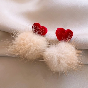 Close-up of red velvet heart earrings with beige plush fur balls on silk fabric