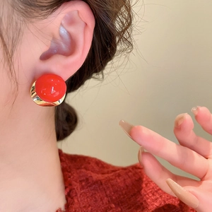 Detail of red spherical earring with golden crescent base worn by a model