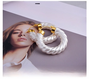Detail view of pearl white spiral hoop earrings with gold clasp on magazine backdrop
