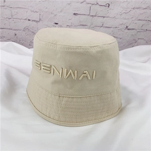 Close-up view of a beige canvas bucket hat with detailed SENWAI letter embroidery