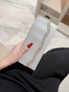 Bolso de noche plateado de tela plisada con decoración de strass sostenido por una modelo