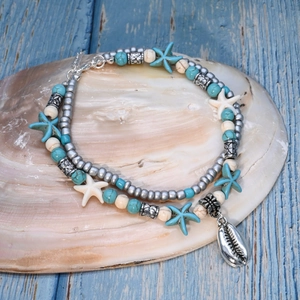 Detail of layered turquoise anklet with sea star and shell pendants on a blue wood background