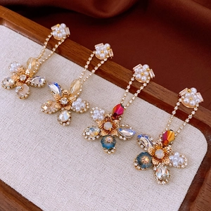 Detailed view of gold flower earrings with crystals, pearls and double chain drop details